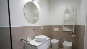 A modern bathroom with a round mirror, a white sink, a bidet, and a towel rack. - B&B CasaLù (Sammichele di Bari)