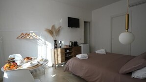 A bedroom with a bed, a dresser, a television, and a dining area with a table set for breakfast. - B&B CasaLù (Sammichele di Bari)