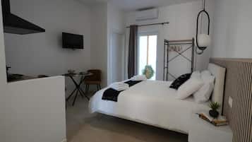 Habitación de hotel con cama, una mesita, una silla, televisión y ventana con cortinas.