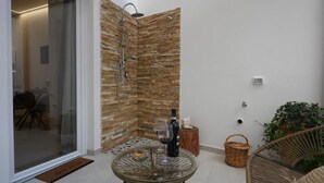 A modern outdoor patio with a glass table, a wicker chair, a stone wall, and a shower area. - B&B CasaLù (Sammichele di Bari)