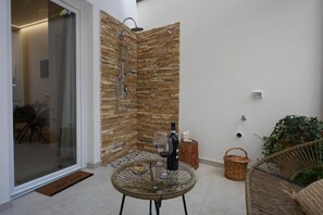 Un patio moderno al aire libre con una mesa de vidrio, una silla de mimbre, un muro de piedra y una zona de ducha.