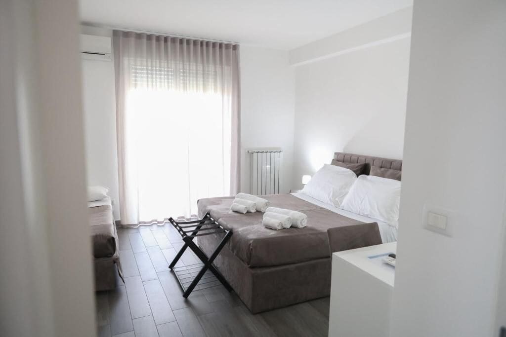 Habitación de hotel con cama, mesita de noche, radiador y ventana con cortinas.