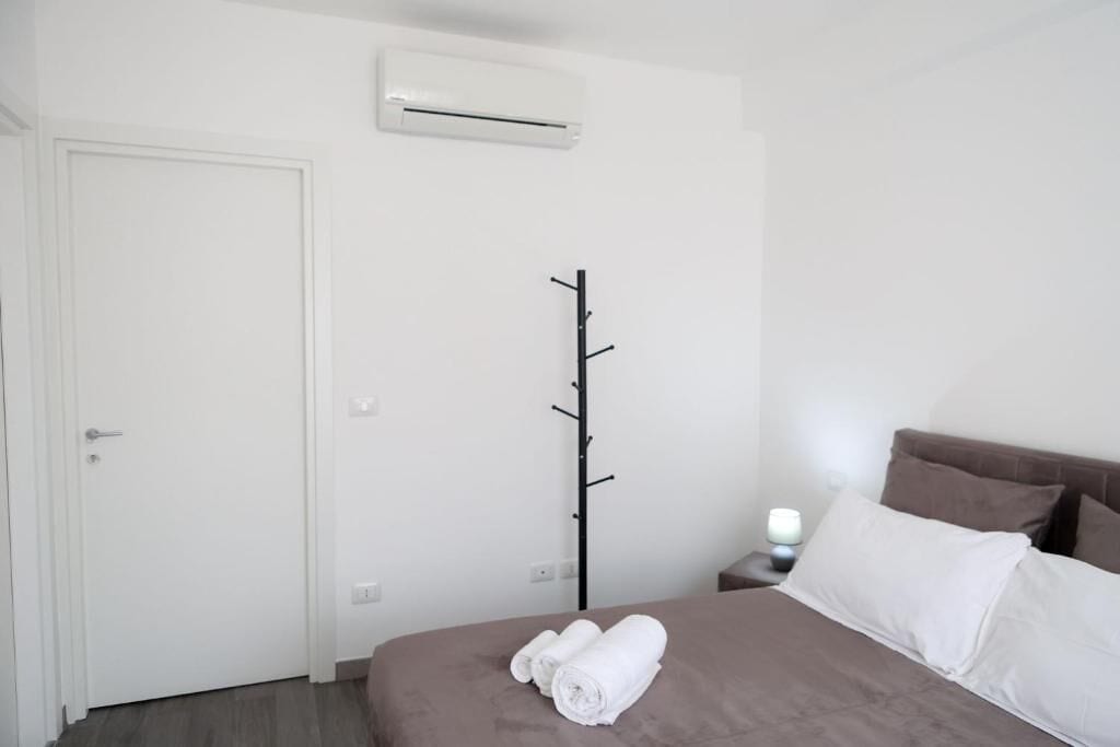 A hotel room with a bed, a coat rack, a bedside table with a lamp, and an air conditioning unit on the wall.