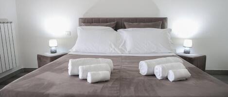 A neatly made bed with white linens and two rolled towels on the bed.