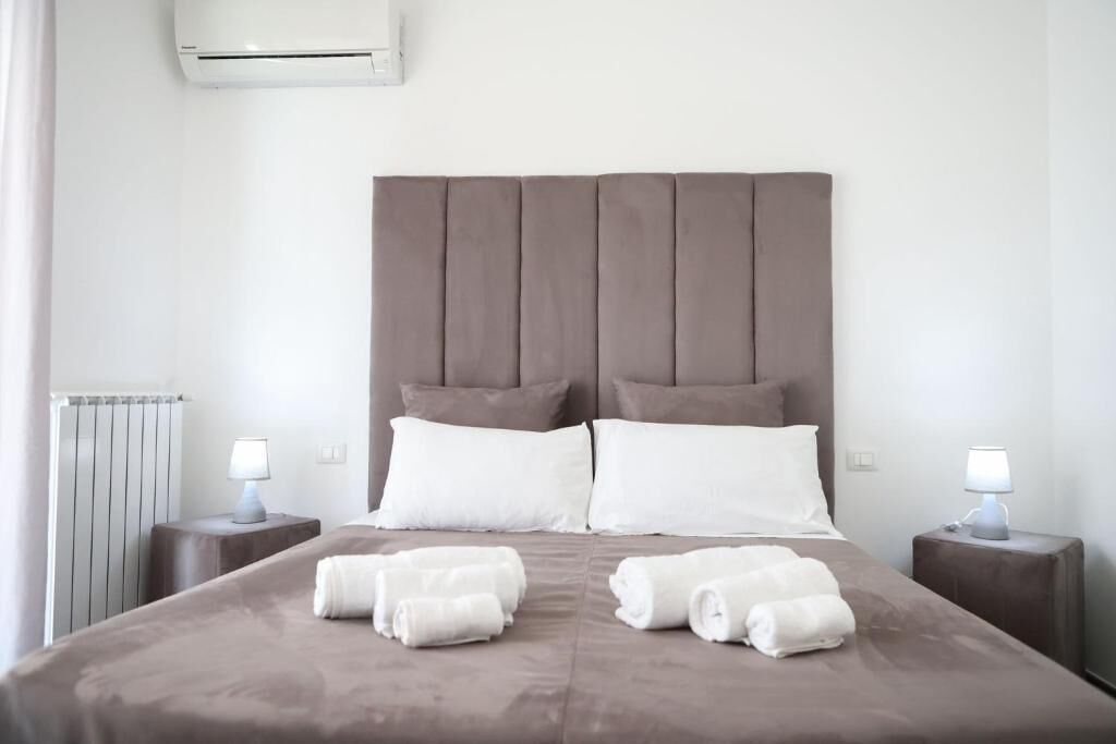 A hotel room with a large bed, two bedside tables with lamps, a radiator, and an air conditioning unit.