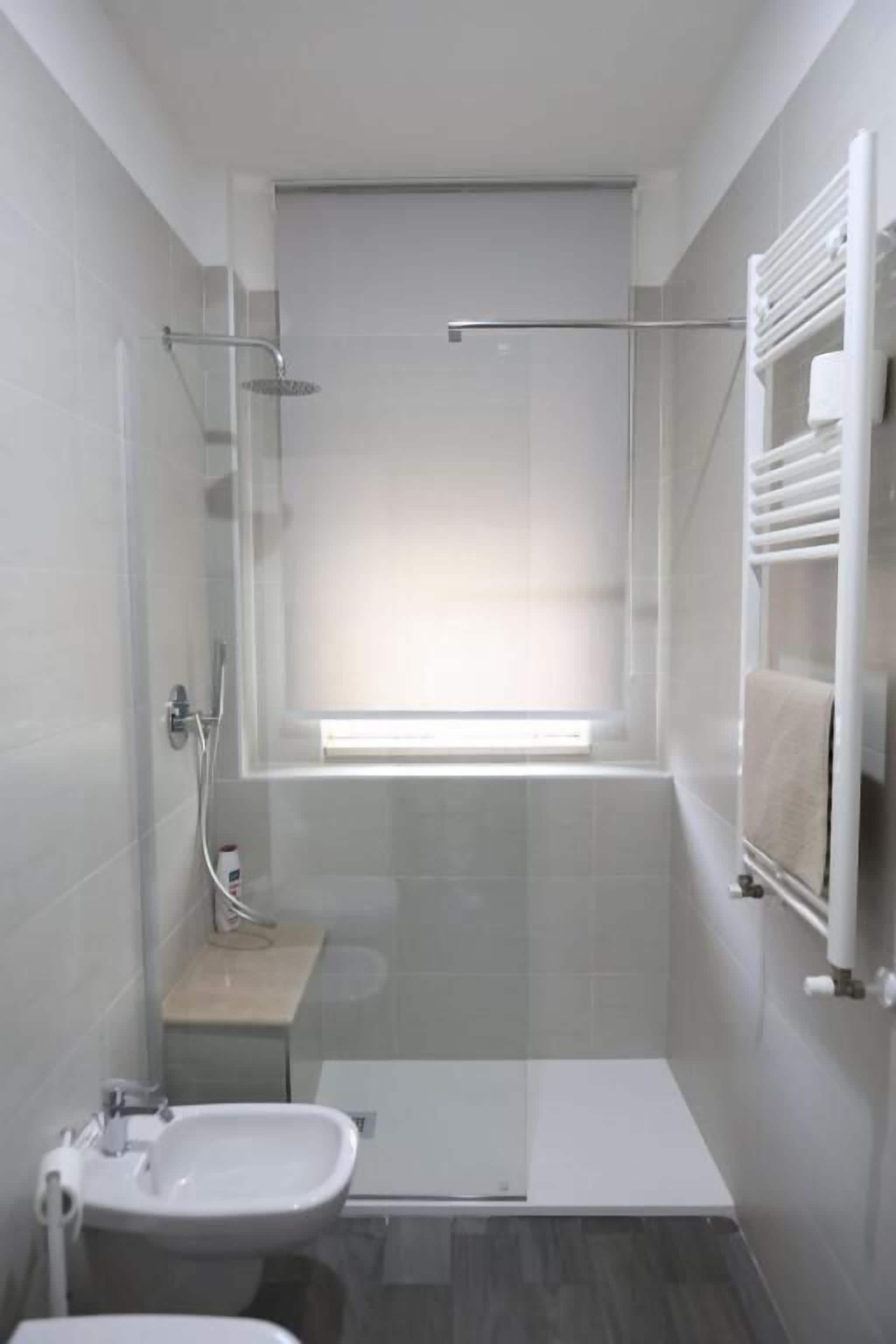 Un bagno moderno con box doccia in vetro, un lavandino piccolo e una finestra sopra la vasca.