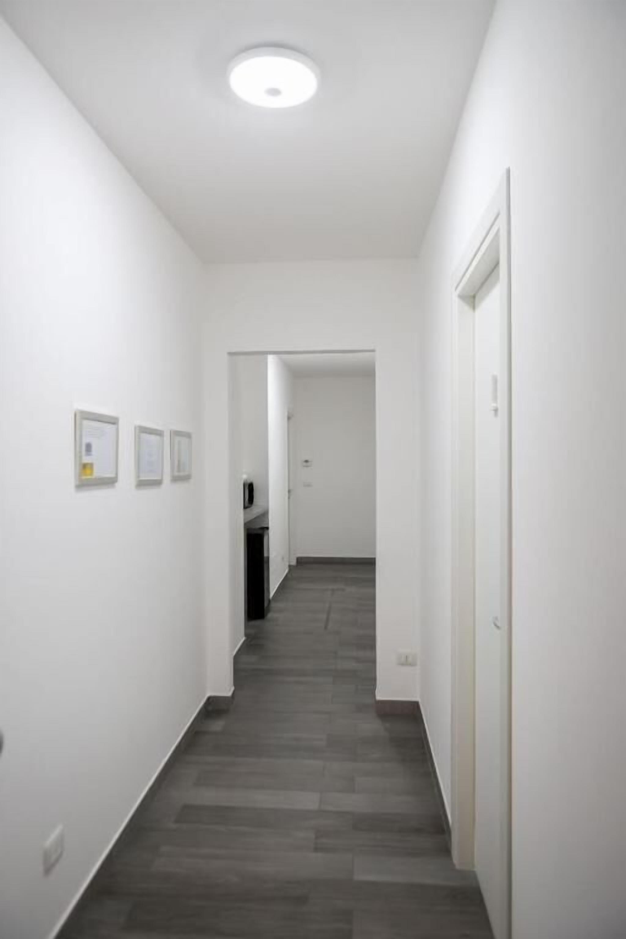A narrow hallway with a wooden floor, white walls, and a door at the end.