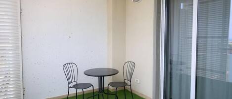 A small outdoor area with a table and two chairs, a sliding glass door, and artificial green turf.