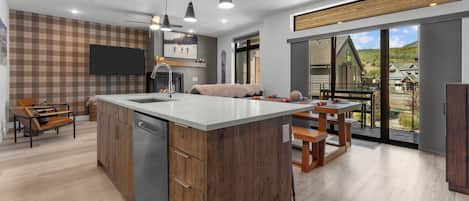 Cocina moderna con una isla central, iluminación colgante y un amplio ventanal con vistas a un área exterior pintoresca.