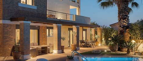 A modern two-story building with a pool, outdoor seating, and a palm tree.
