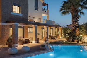 Un edificio moderno de dos pisos con piscina, mobiliario exterior y una palmera.