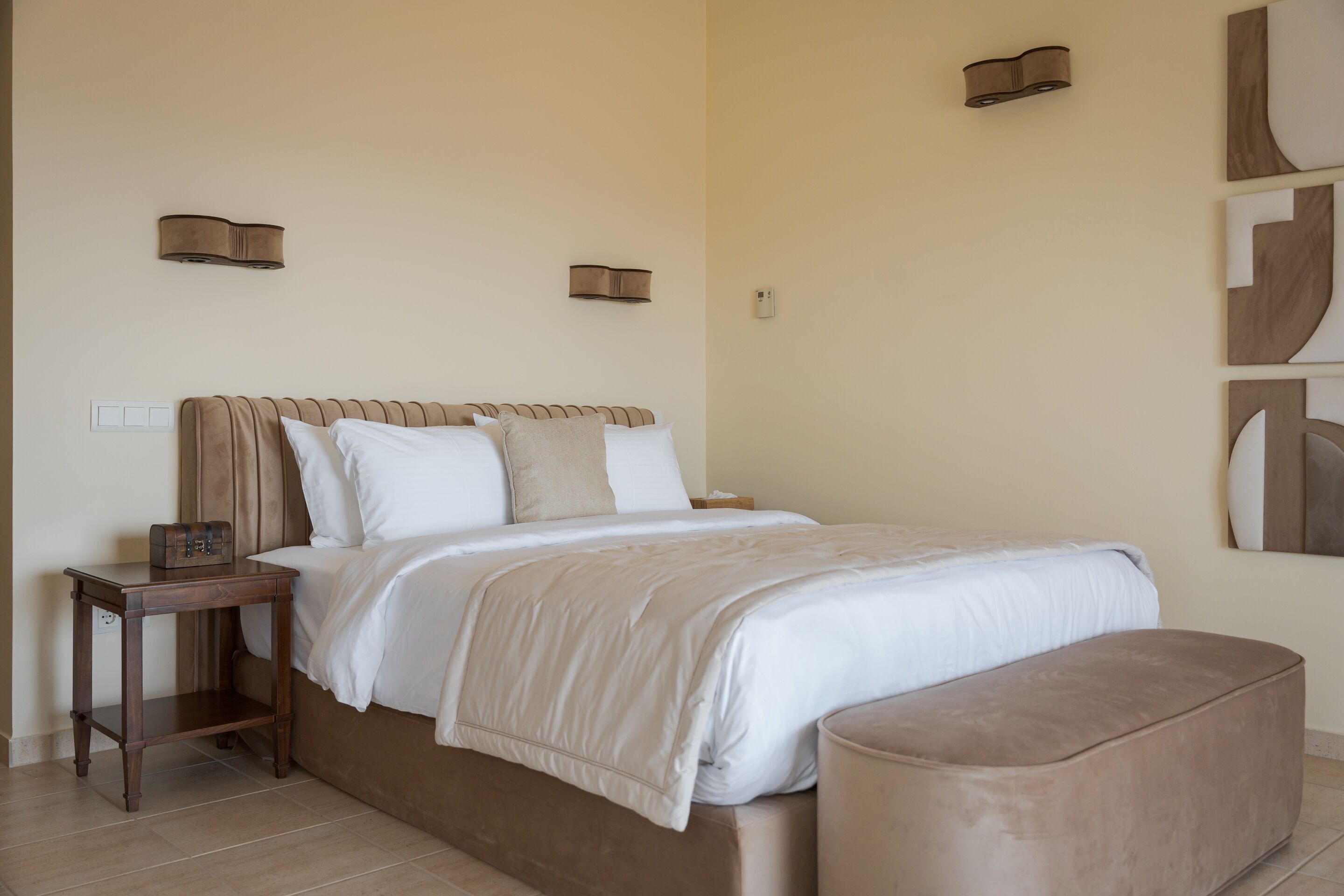 A bedroom with a bed, bedside tables, a bench, and wall-mounted lighting.