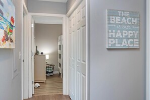 A hallway with a door leading to a room, a wall with a sign that reads 'THE BEACH is our HAPPY PLACE', and a painting on the wall. - Cottage By The Sea (Port St. Joe)