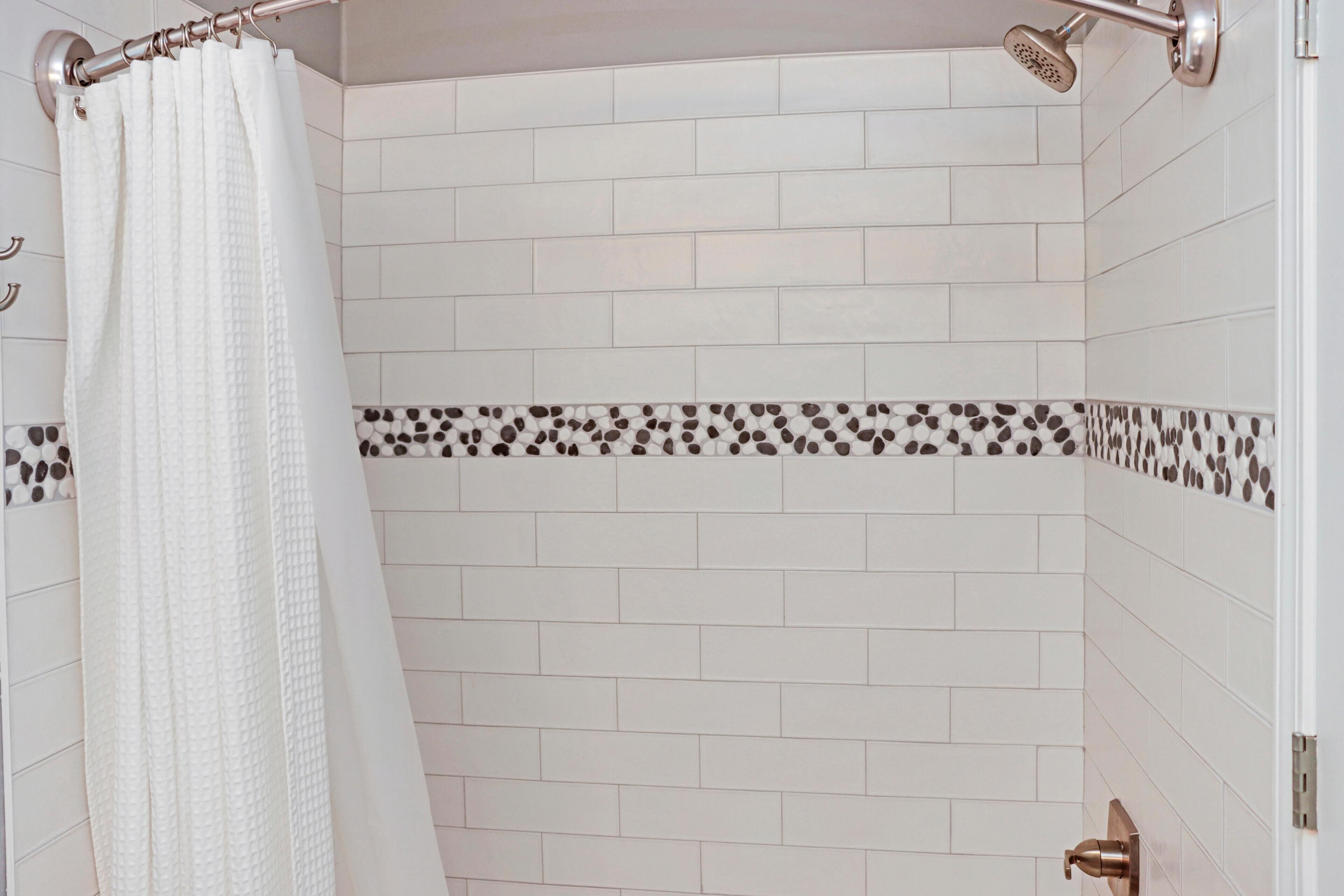 A shower with white tiles and a pebble-patterned border.