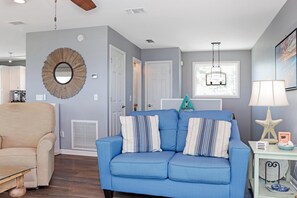A living room with a blue sofa, a beige armchair, and a wooden coffee table. There is a round mirror on the wall, a starfish decoration, and a framed picture. - Cottage By The Sea (Port St. Joe)