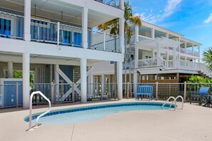 Ein mehrstöckiges Hotel mit Poolbereich, Außenbestuhlung und blauem Himmel.