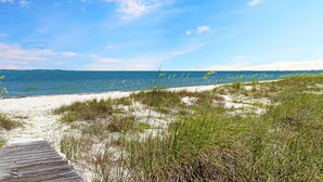 Ein Strand mit einer hölzernen Promenade, die zum Wasser führt, umgeben von Sand und Vegetation.