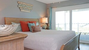A bedroom with a large bed, a bedside table, a wall-mounted lamp, and a view of the outdoors through a window.