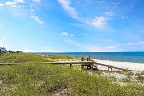 A beach with a wooden boardwalk leading to the water, grassy dunes, and a clear blue sky. - Cottage By The Sea (Port St. Joe)
