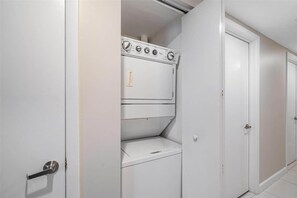 A laundry room with a stacked washer and dryer, a door, and a tiled floor. - Icon Brickell 2BR · Panoramic Bay Views, Sleeps 6 (Miami)