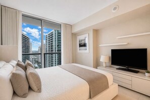 A modern hotel room with a large bed, a flat-screen TV, and a city view. - Icon Brickell 2BR · Panoramic Bay Views, Sleeps 6 (Miami)