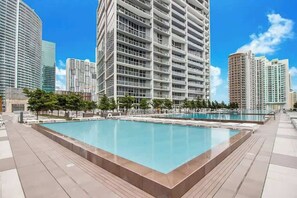 A modern building with a large rectangular pool surrounded by a paved area and trees. - Icon Brickell 2BR · Panoramic Bay Views, Sleeps 6 (Miami)