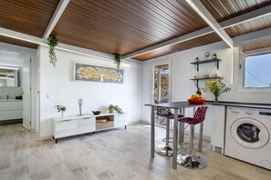 A modern kitchen with a central island, a washing machine, and a dining area with chairs.