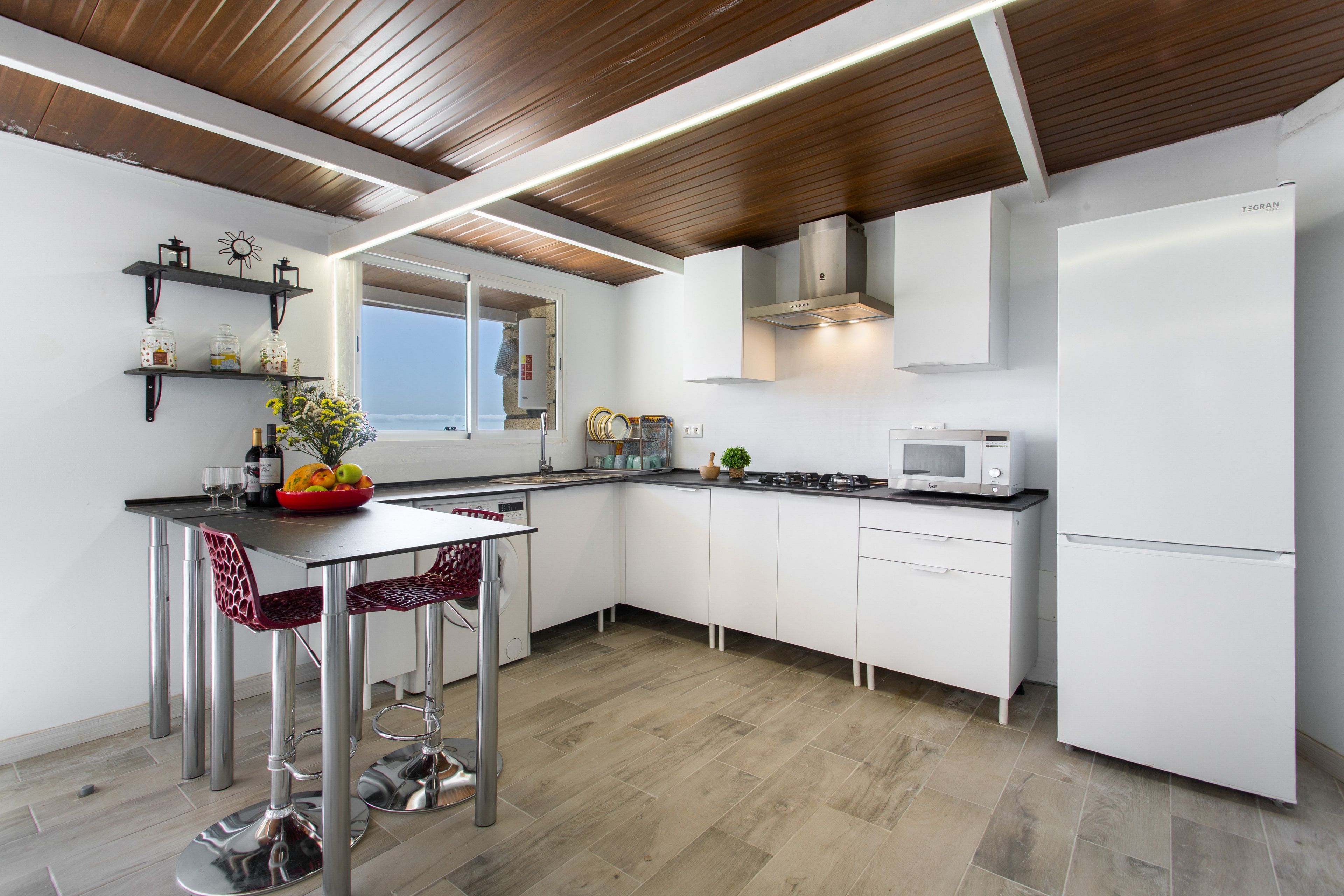 A modern kitchen with white cabinetry, stainless steel appliances, and a wooden ceiling.