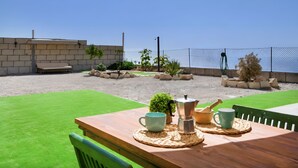 Eine Außenpatio mit einem Holztisch, Stühlen und Blick aufs Meer.