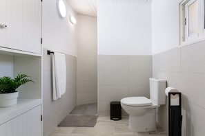 Et lille, hvidt badeværelse med toilet, vask, håndklædestang og en potteplante.