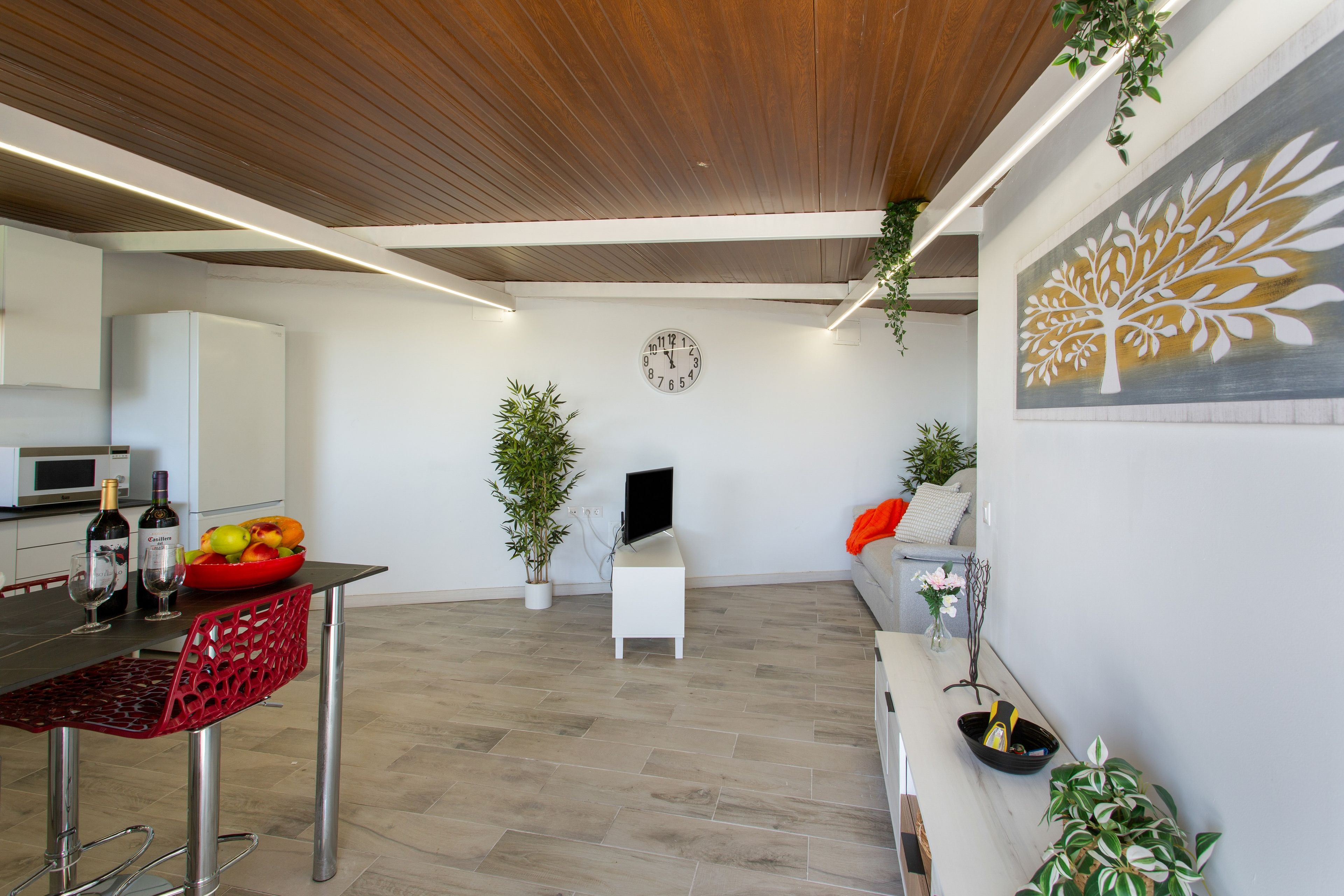 A modern kitchen with a dining area, a flat-screen TV, and a fruit bowl.