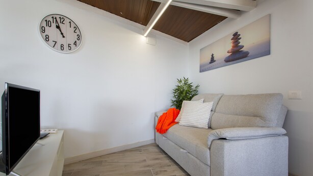 Ein Wohnzimmer mit grauem Sofa, einem Flachbildfernseher, einer Wanduhr und einem Gemälde eines Zen-Gartens.