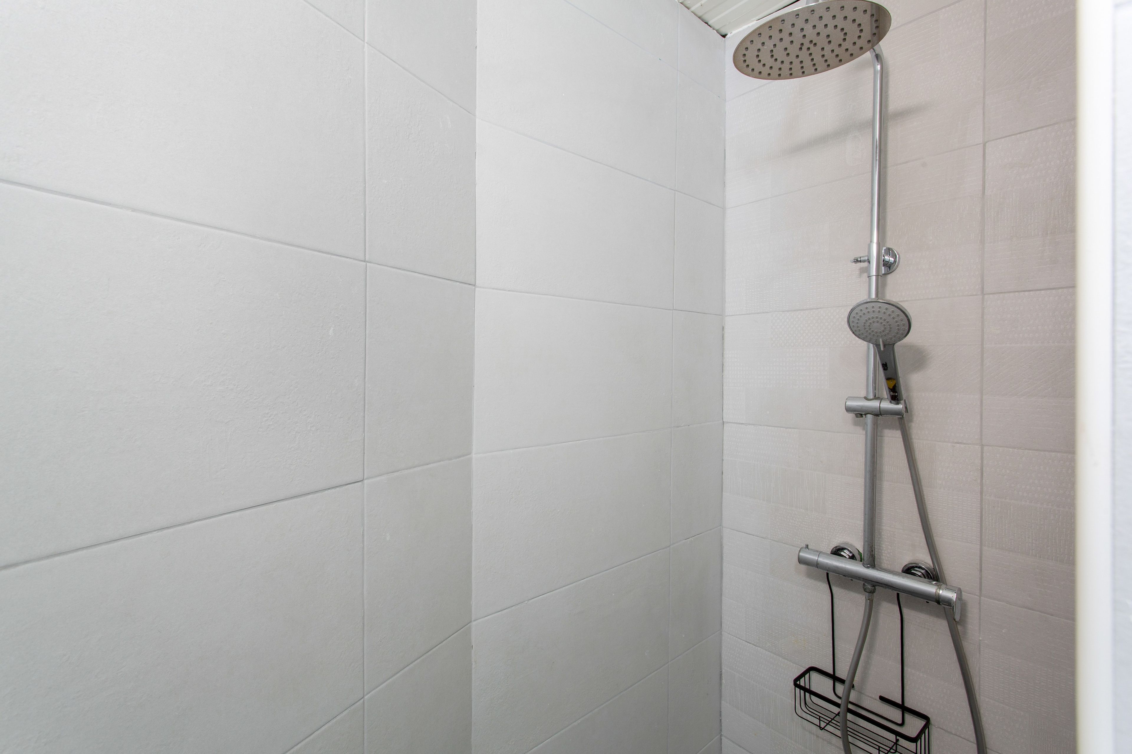Eine Dusche mit Duschkopf zum Handgebrauch und einer an der Wand montierten Armatur.