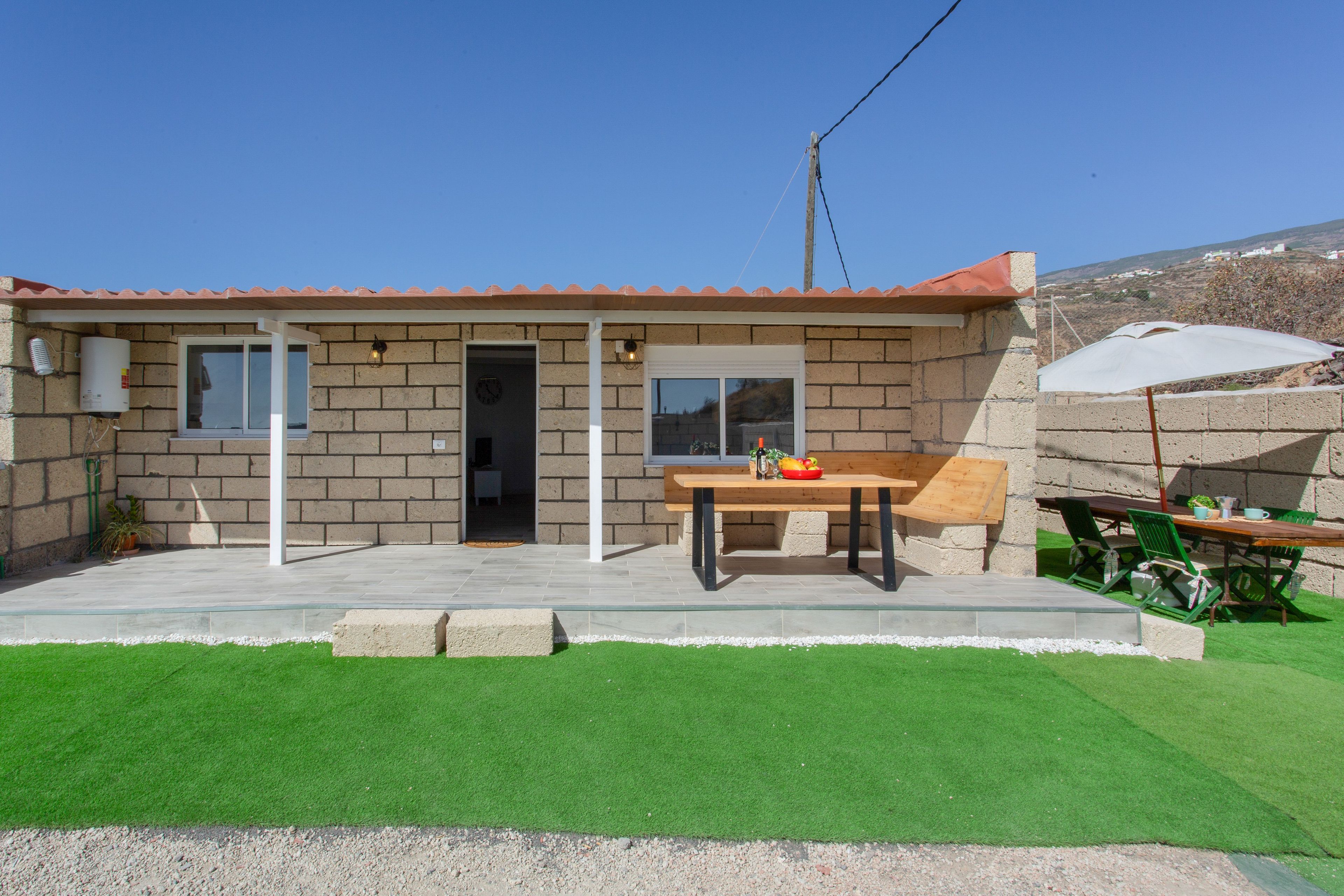 Una casa con techo de tejas, puerta principal, ventana y patio con mesa y sillas.