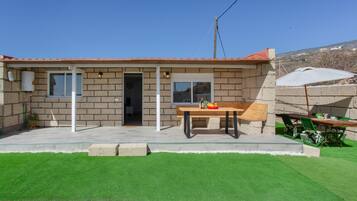 Una casa con techo de tejas, puerta principal, ventana y patio con mesa y sillas.