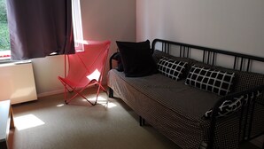 A room with a bed, a red chair, a window with curtains, and a radiator.