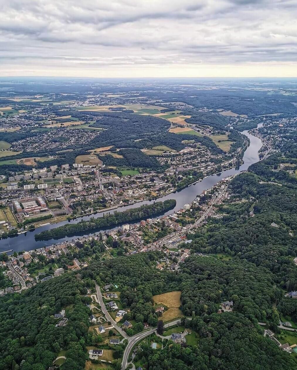 Ein Luftbild einer Stadt, durch die ein Fluss fließt, umgeben von Grünflächen und Wohngebieten.