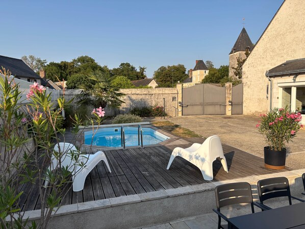 A backyard with a swimming pool, a wooden deck, and outdoor seating.