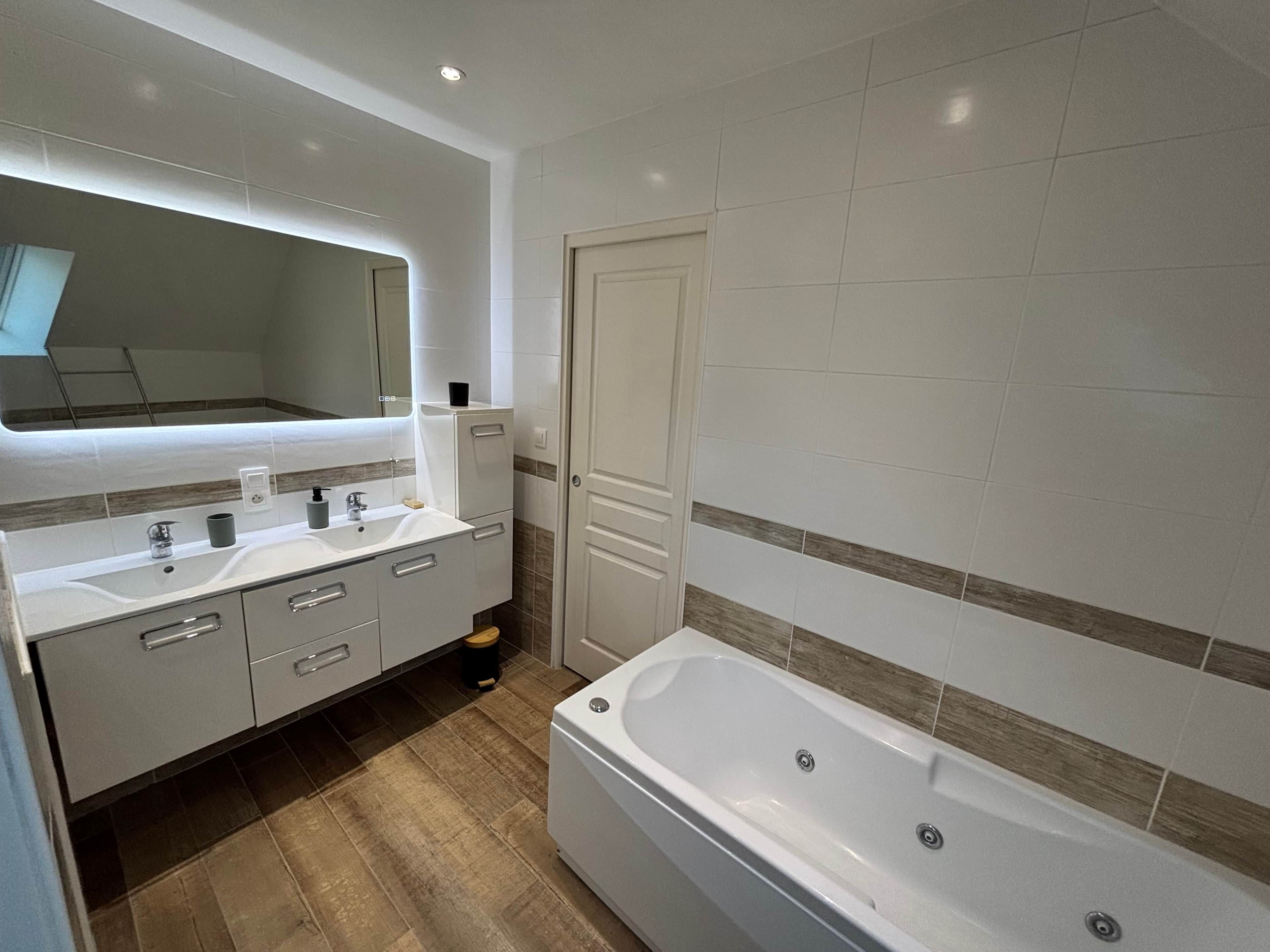 Een moderne badkamer met een groot bad, een wastafel met spiegel, en een deur naar een andere kamer.