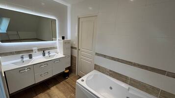 Een moderne badkamer met een groot bad, een wastafel met spiegel, en een deur naar een andere kamer.