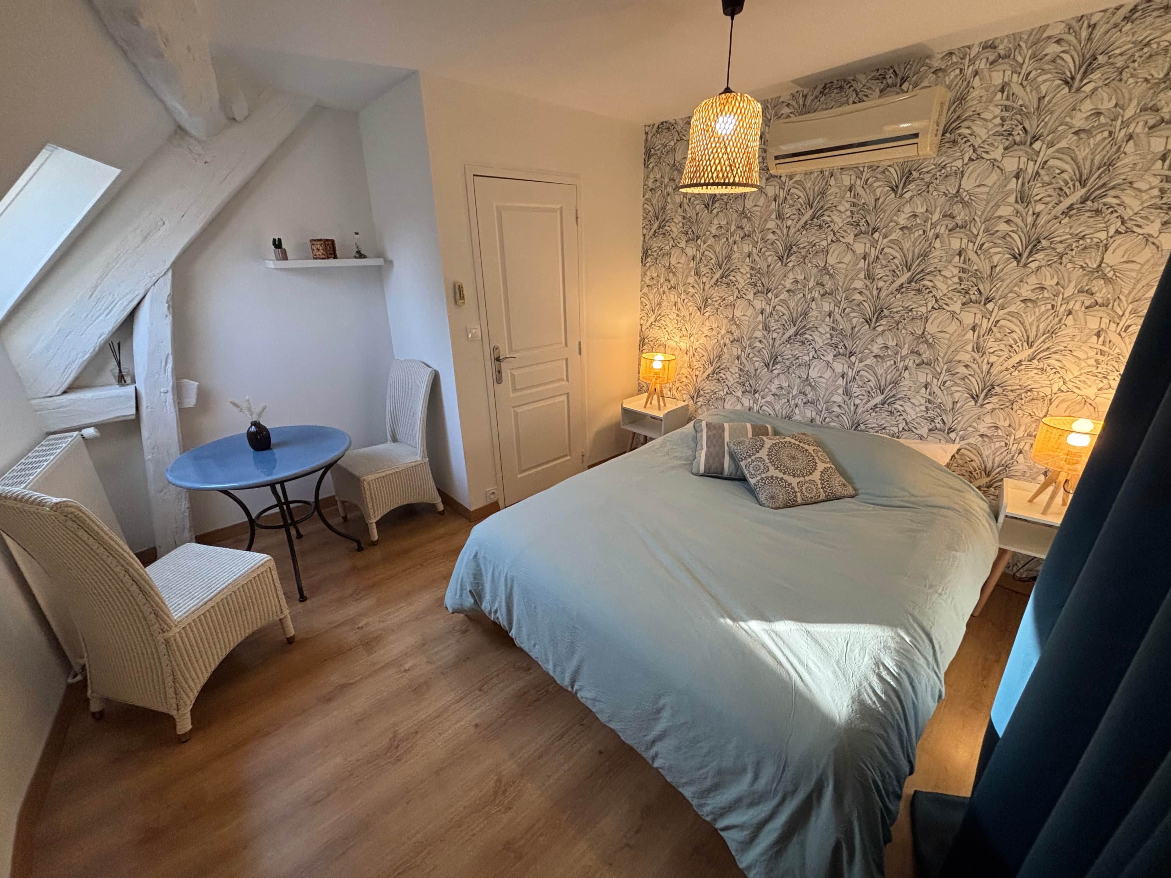 Une chambre à coucher comprenant un lit, deux chaises, une petite table et un mur décoratif.