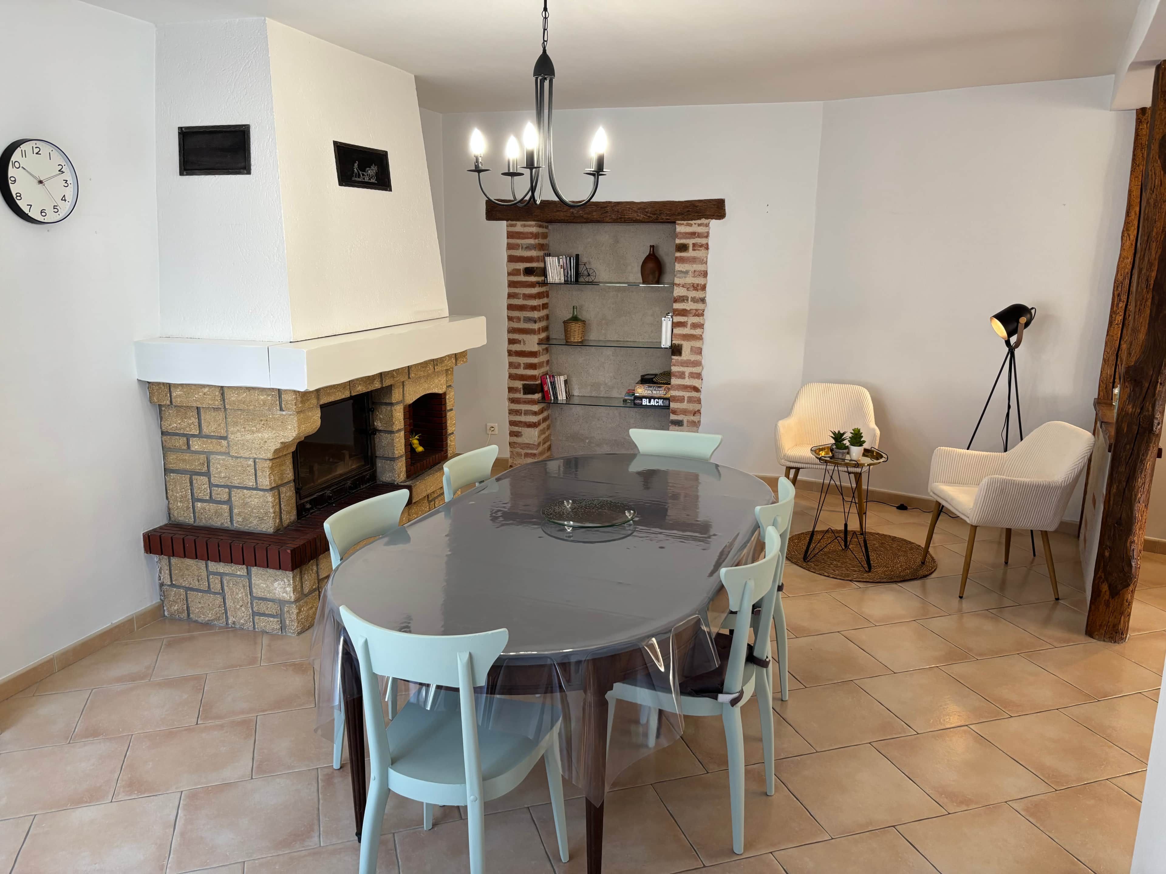 Uma sala de jantar com mesa redonda, cadeiras, lareira e um candelabro.