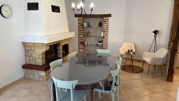 Uma sala de jantar com mesa redonda, cadeiras, lareira e um candelabro.