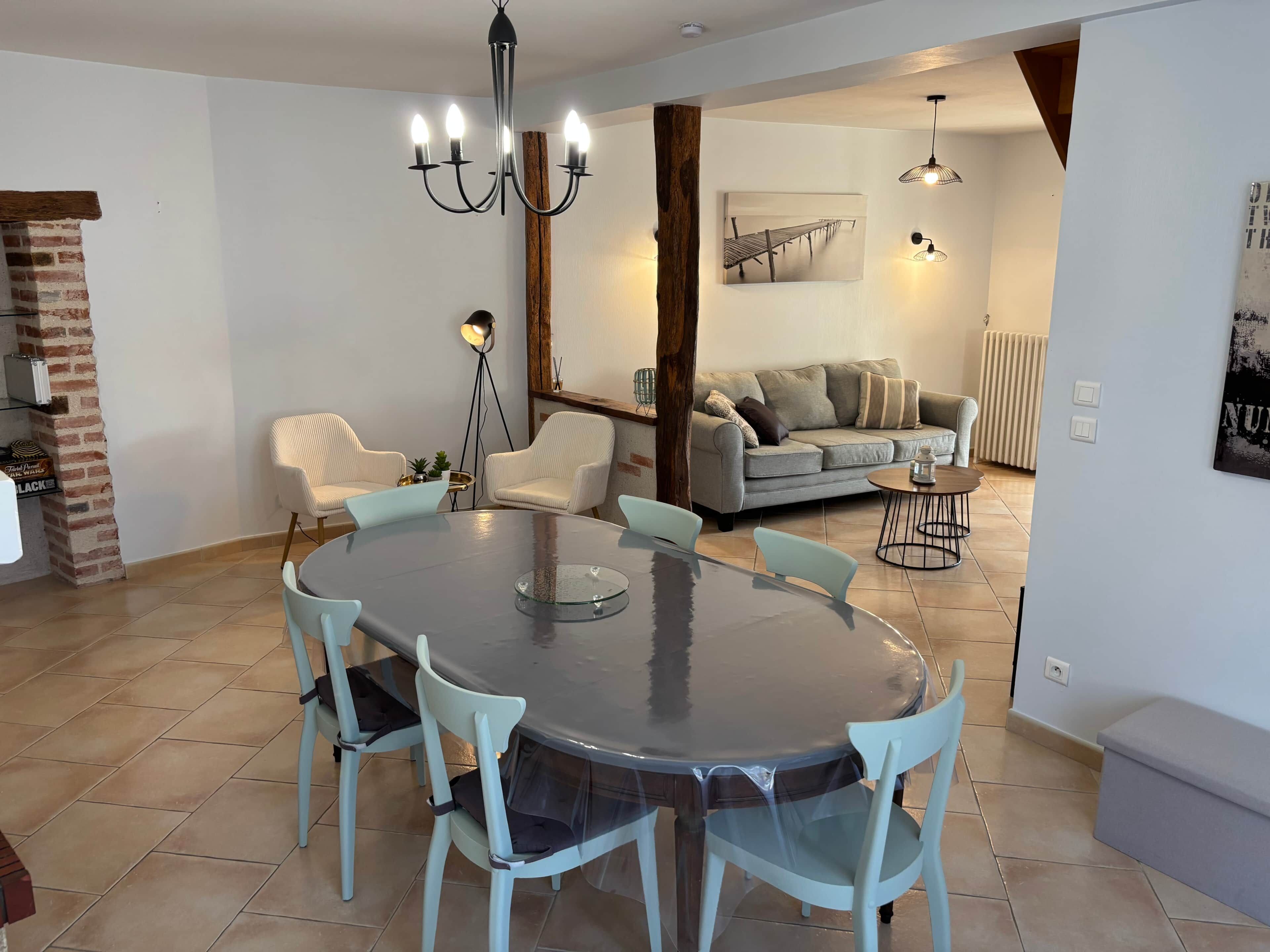 Un coin repas avec une table ronde et des chaises, un lustre et un canapé en arrière-plan.