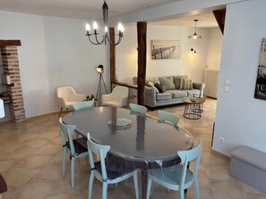 A dining area with a round table and chairs, a chandelier, and a sofa in the background.