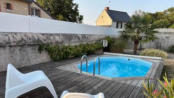 A swimming pool with a wooden deck, a white chair, and a white lounge chair.