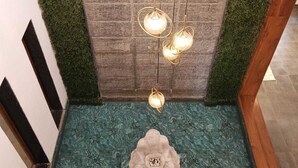 Una scala con una parete verde e strutturata, una scultura floreale decorativa alla base e una serie di luci a sospensione.
