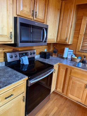 A kitchen with wooden cabinets, a stainless steel microwave, a black stove, and a granite countertop. - A Bear's Kind of Fun (Sevier County)