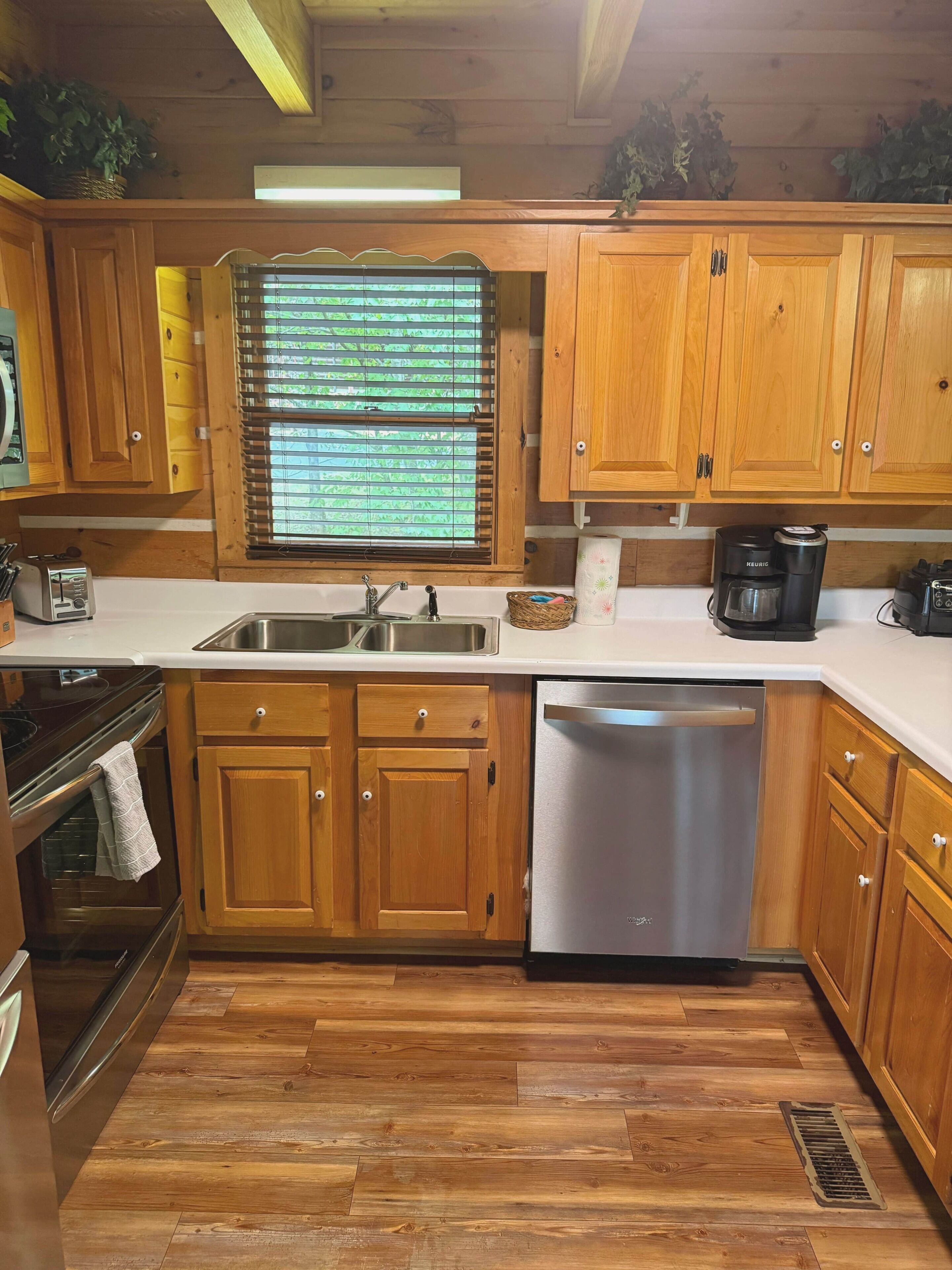 A kitchen with wooden cabinets, a stainless steel sink, a dishwasher, and a Keurig coffee maker.