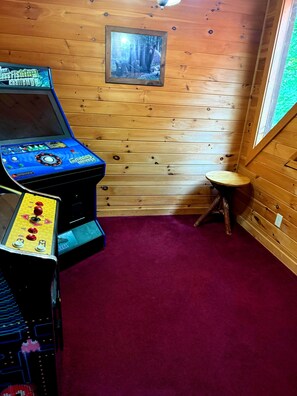 Ett rum med en väggpanel av trä, en inramad tavla, en liten pall och en spelmaskin.